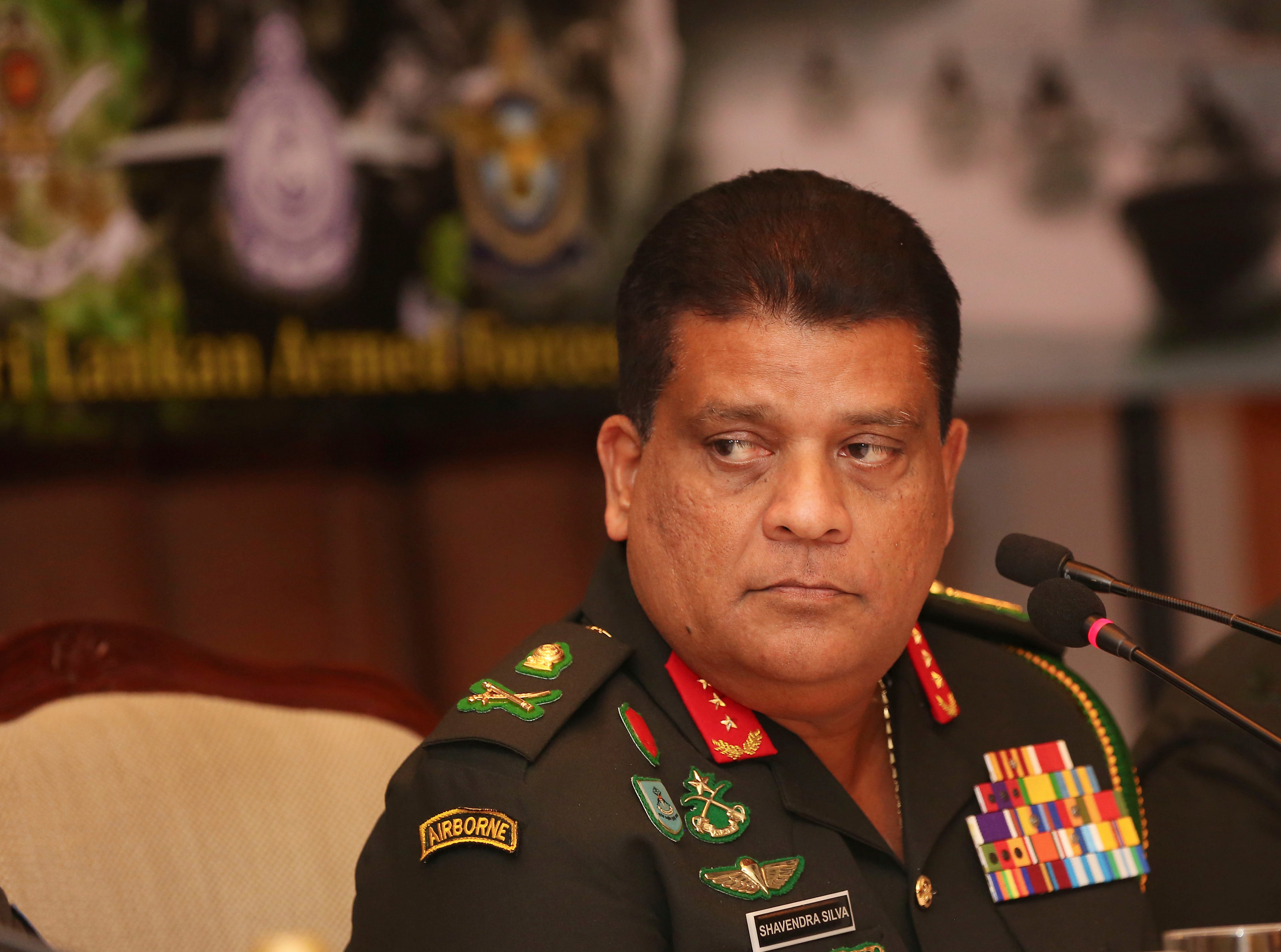 A uniformed military officers sits in front of microphones