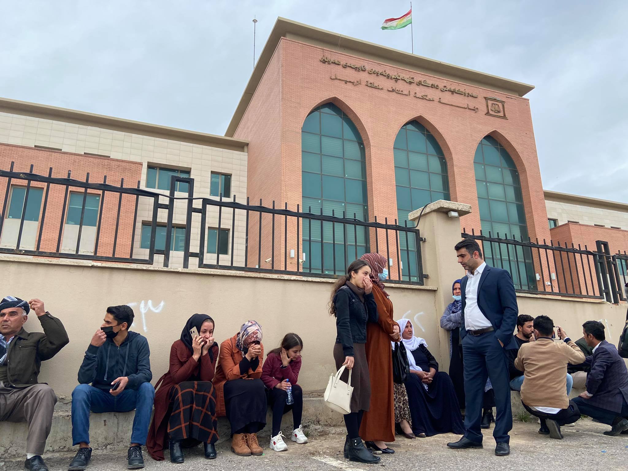 خێزانی چالاکوانان و ڕۆژنامەنوسەکان لە ڕۆژی دادگایکردنی ١٦ی شوباتی ٢٠٢١، دانیشتوون لە دەرەوەی سەرۆکایەتی داداگای تێهەڵچوونەوەی ناوچەی هەولێر.