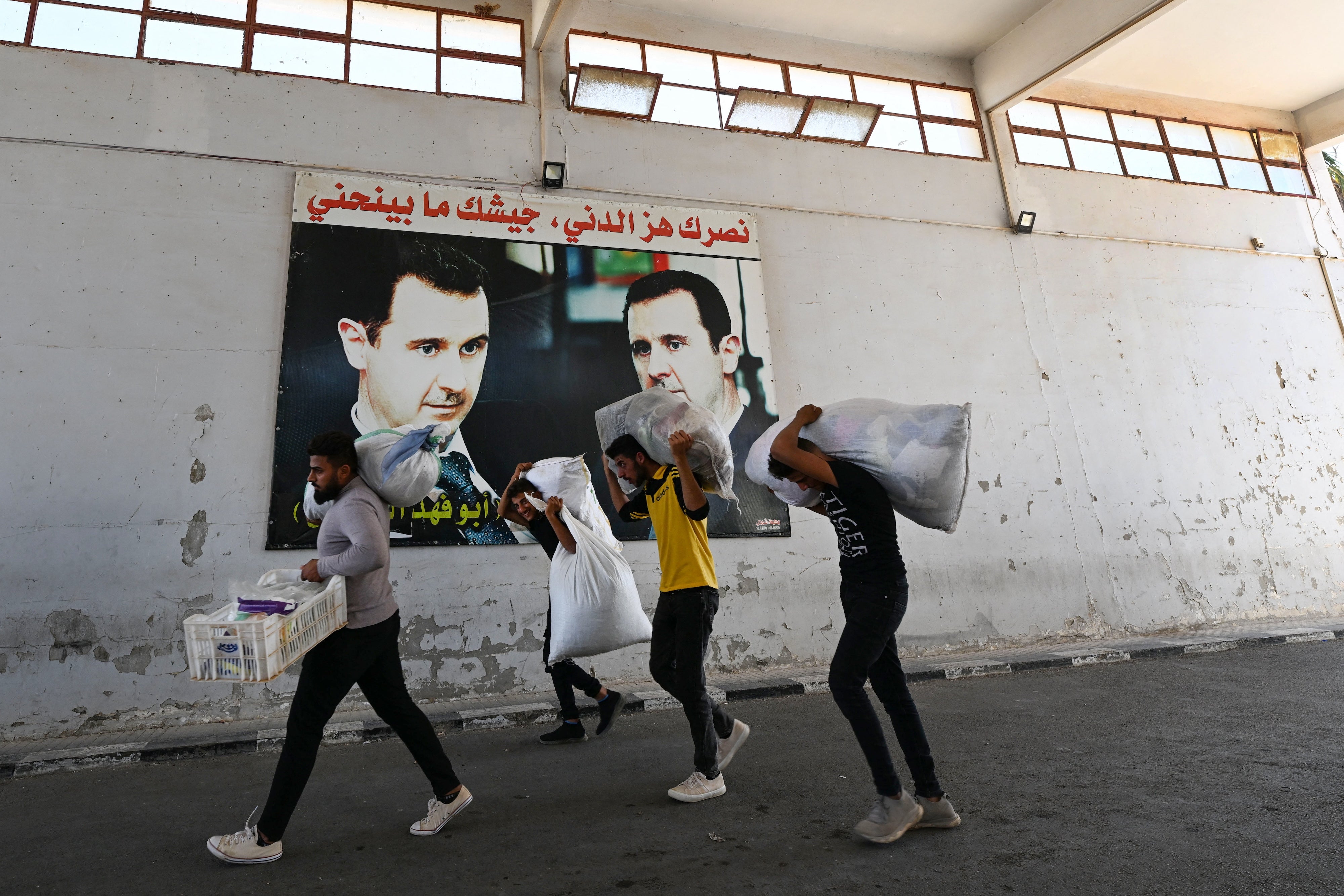 نازحون يمشون أمام ملصقات للرئيس بشار الأسد أثناء دخولهم سوريا من لبنان عبر معبر جوسيه، 2 أكتوبر/تشرين الأول 2024.