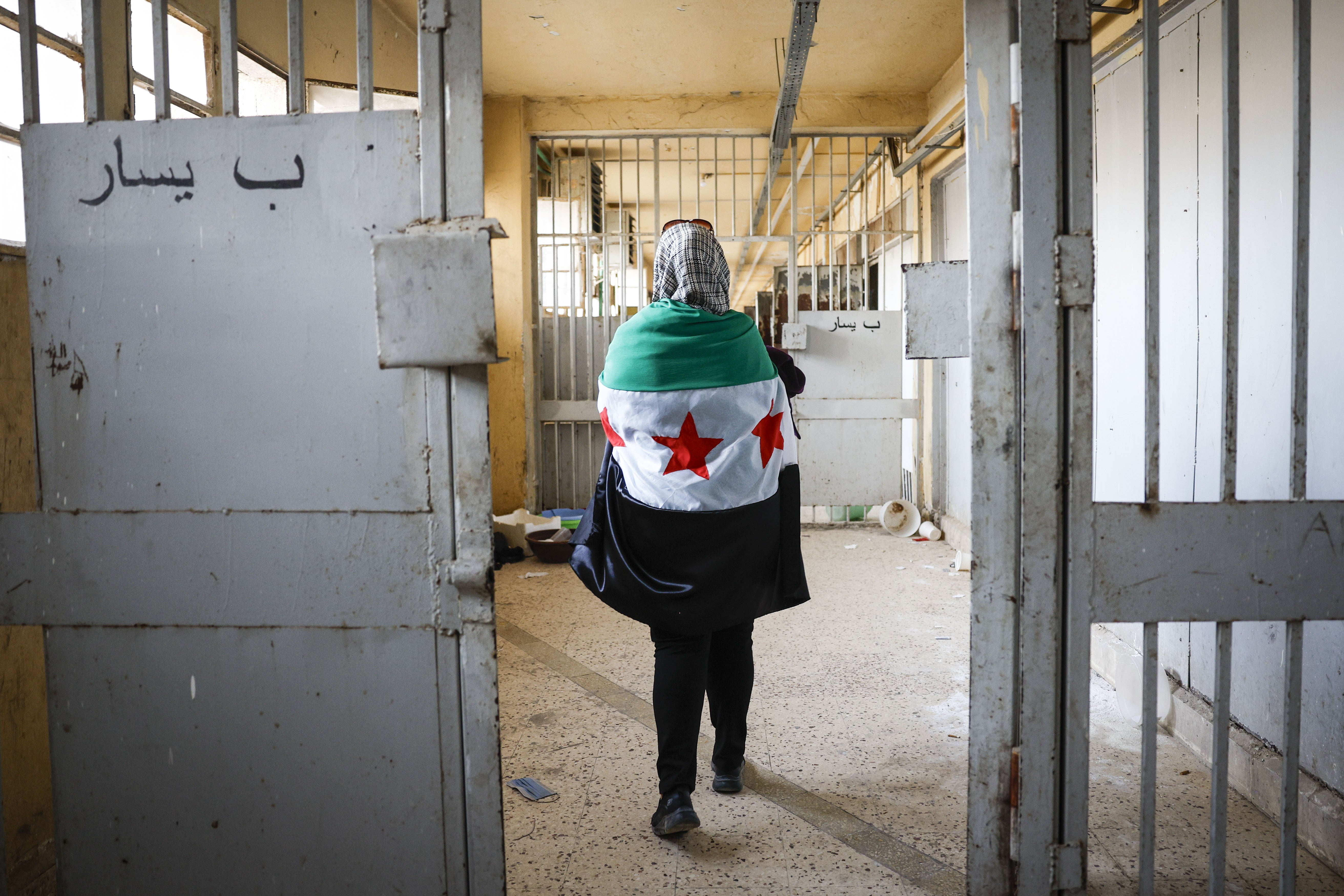 Une femme portant le drapeau syrien sur son dos marchait dans un couloir de la prison de Sednaya, près de Damas, en Syrie, le 12 décembre 2024, quatre jours après le renversement du président Bachar al-Assad et sa fuite vers Moscou. 