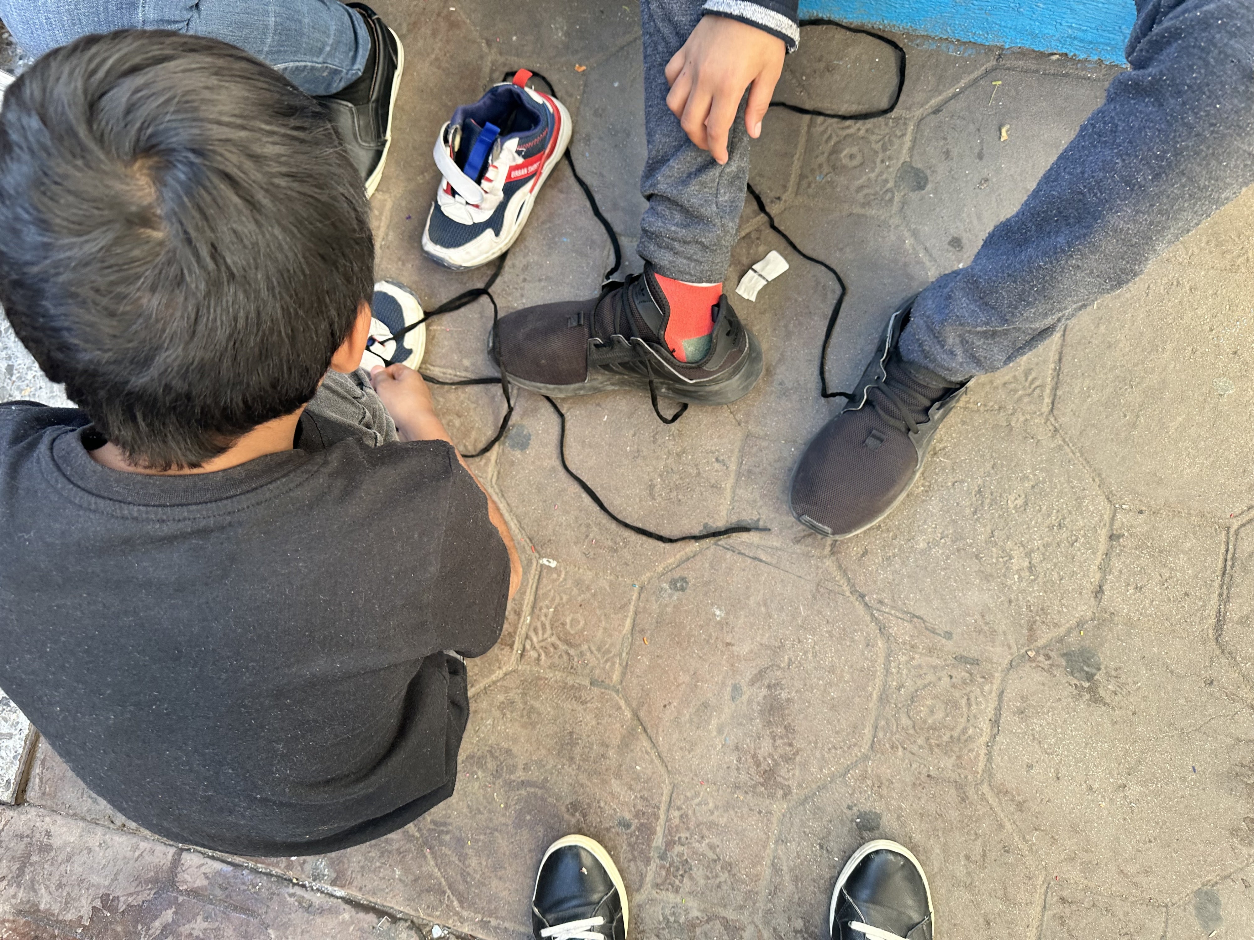 Niñas y niños deportados poco antes se ponen los cordones que les entregaron voluntarios de Good Samaritans de Tucson y Green Valley, Arizona.