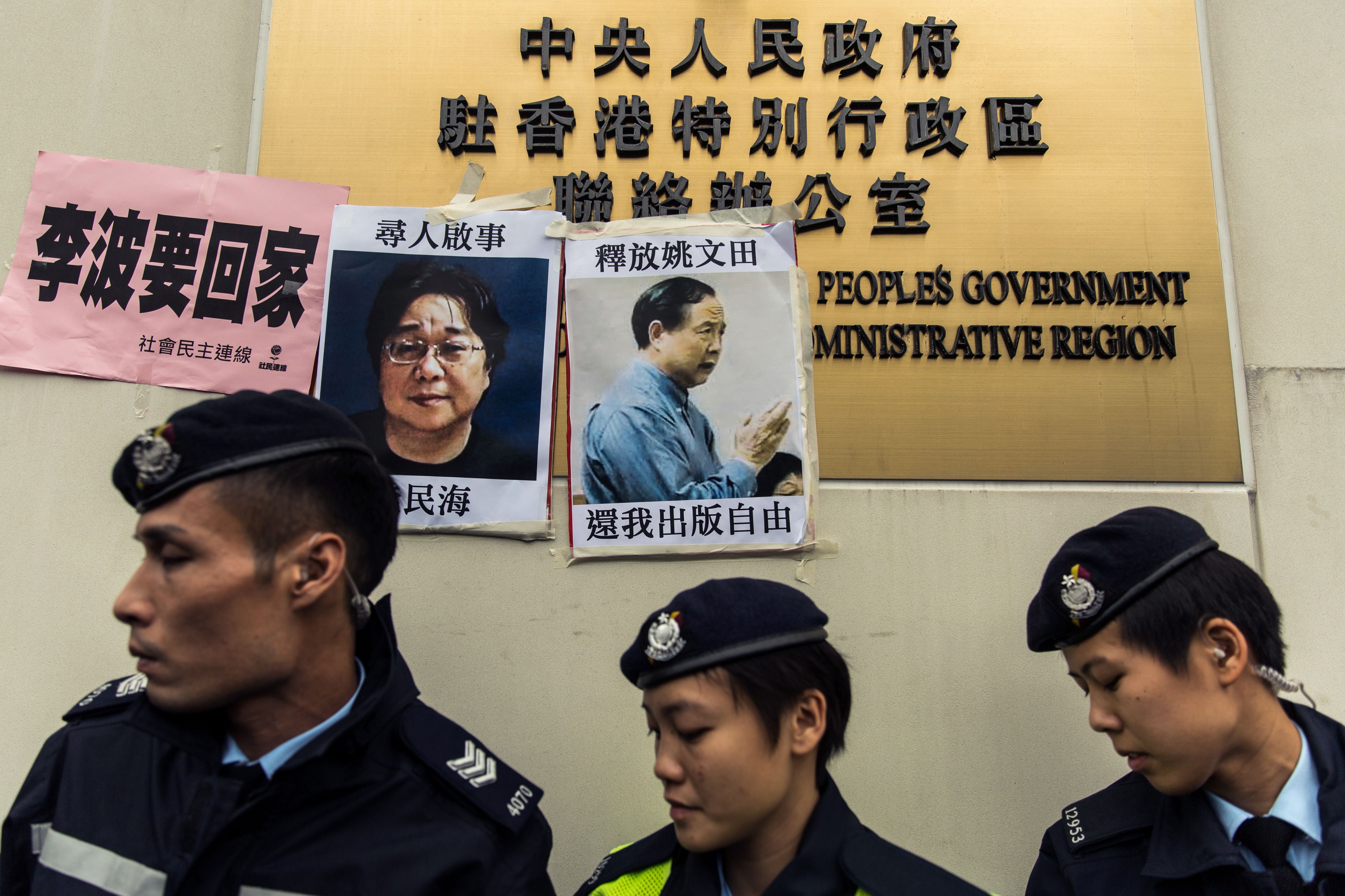 Poliser passerar efterlysningsaffischer för den svenske förläggaren Gui Minhai (t.v.) och den Hongkong-baserade förläggaren Yau Wentian, uppsatta på skylten till Kinas kontaktkontor i Hongkong den 3 januari 2016.