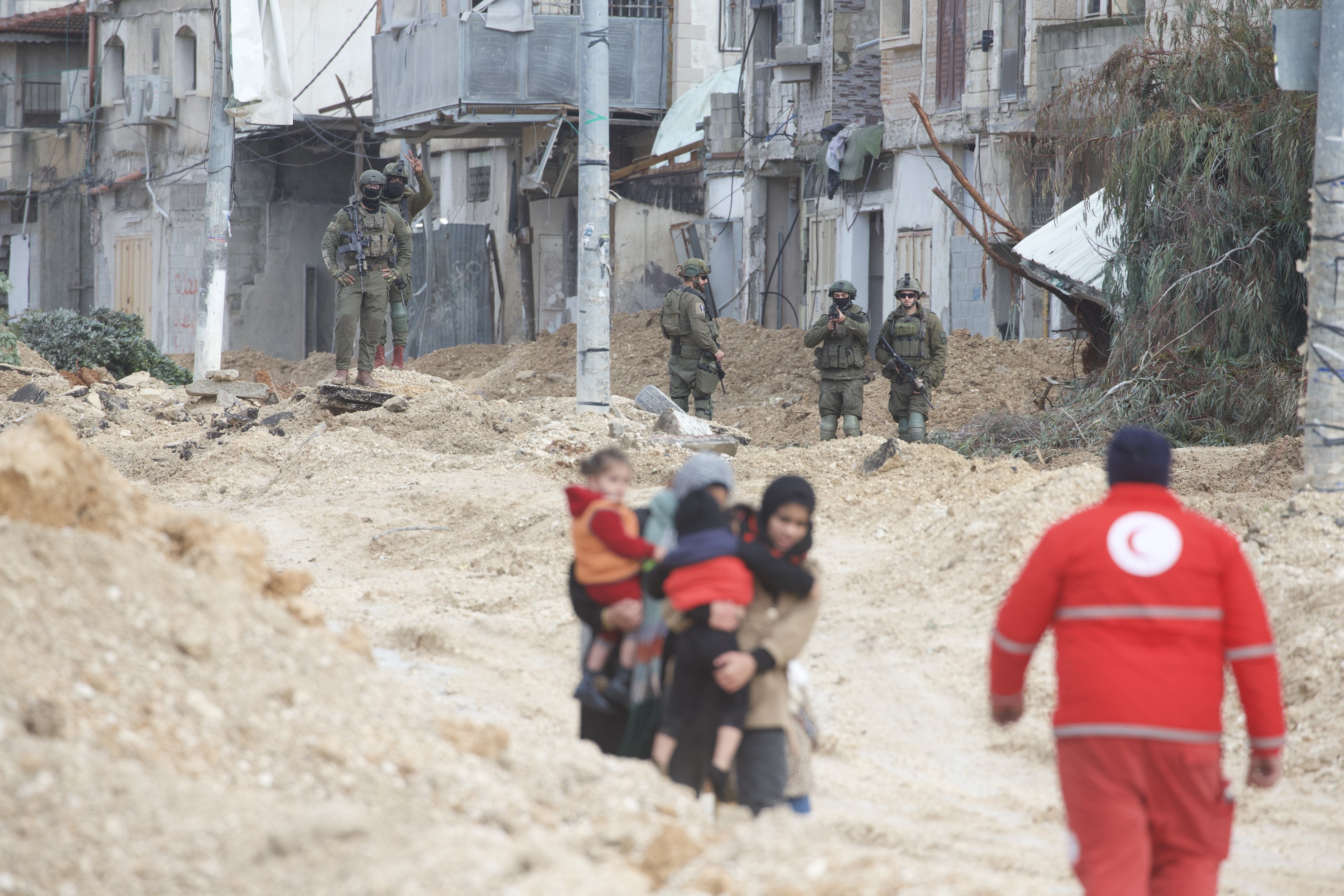 Frauen tragen Kinder, während israelische Streitkräfte sie am 10. Februar 2025 gewaltsam aus dem Flüchtlingslager Nur Shams im nördlichen Westjordanland vertreiben. Israelische Soldaten sehen zu, einer mit erhobener Waffe. © 2025 Wahaj Bani Moufleh