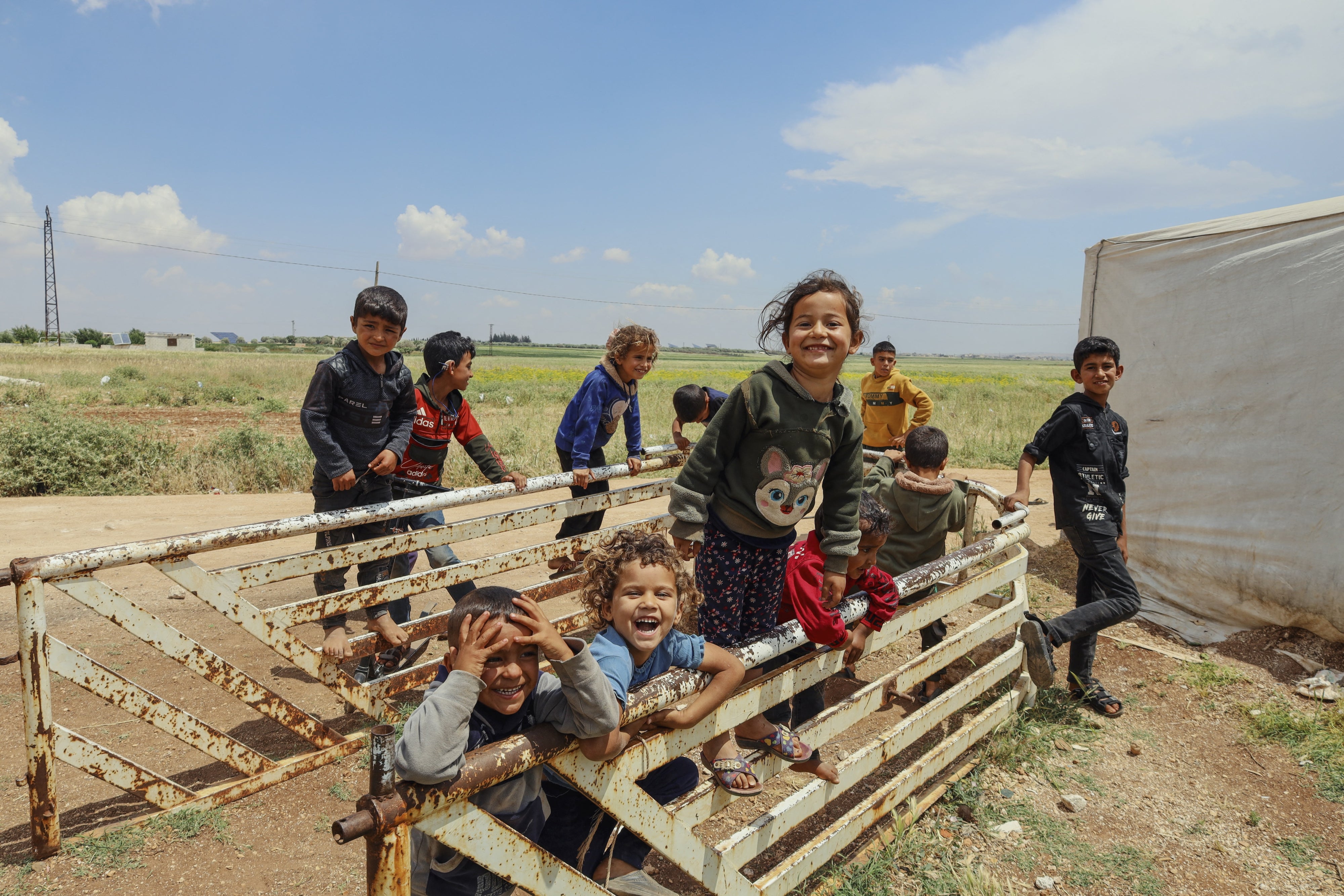 Des enfants syriens déplacés rient et jouent parmi les tentes provisoires installées après la chute du gouvernement de Bachar al-Assad près d'Idlib, en Syrie, le 15 mai 2025.