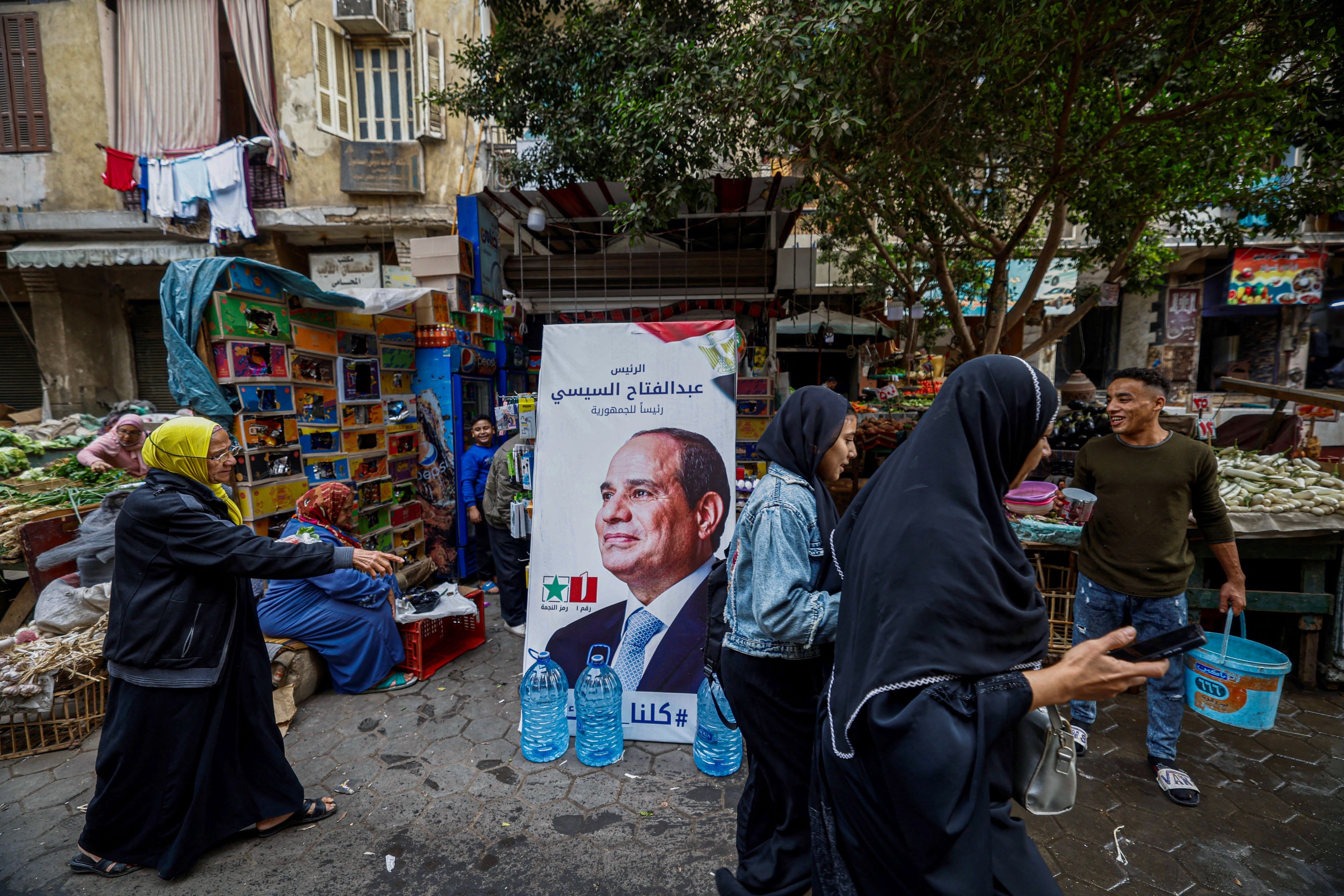 أشخاص يسيرون بجوار لافتة للحملة الانتخابية للرئيس المصري عبد الفتاح السيسي في أحد أسواق القاهرة في 7 ديسمبر/كانون الأول 2023، قبيل الانتخابات الرئاسية.
