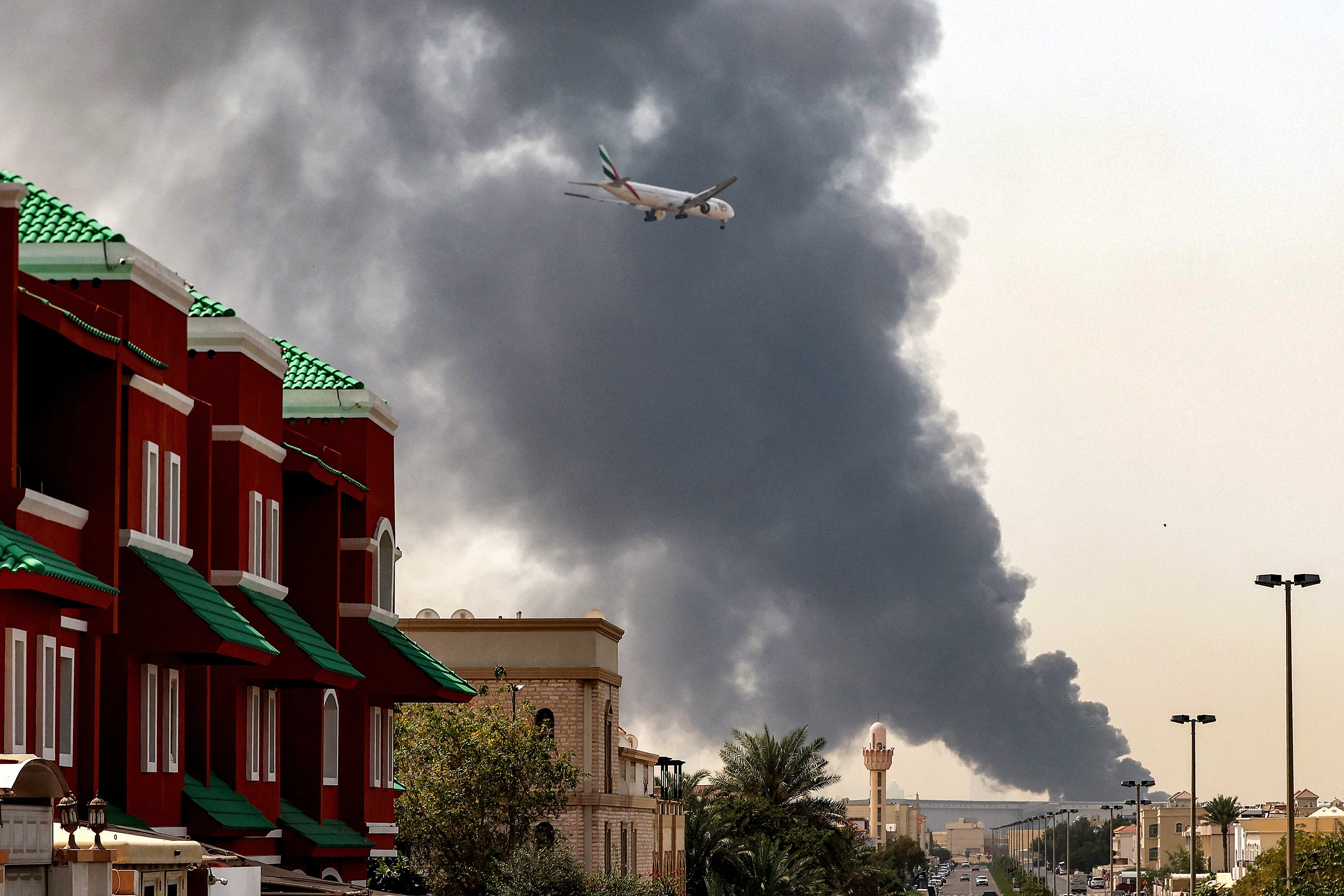 An Emirates aircraft prepares for landing as a smoke plume rises from an ongoing fire near Dubai International Airport, UAE, on March 16, 2026. 