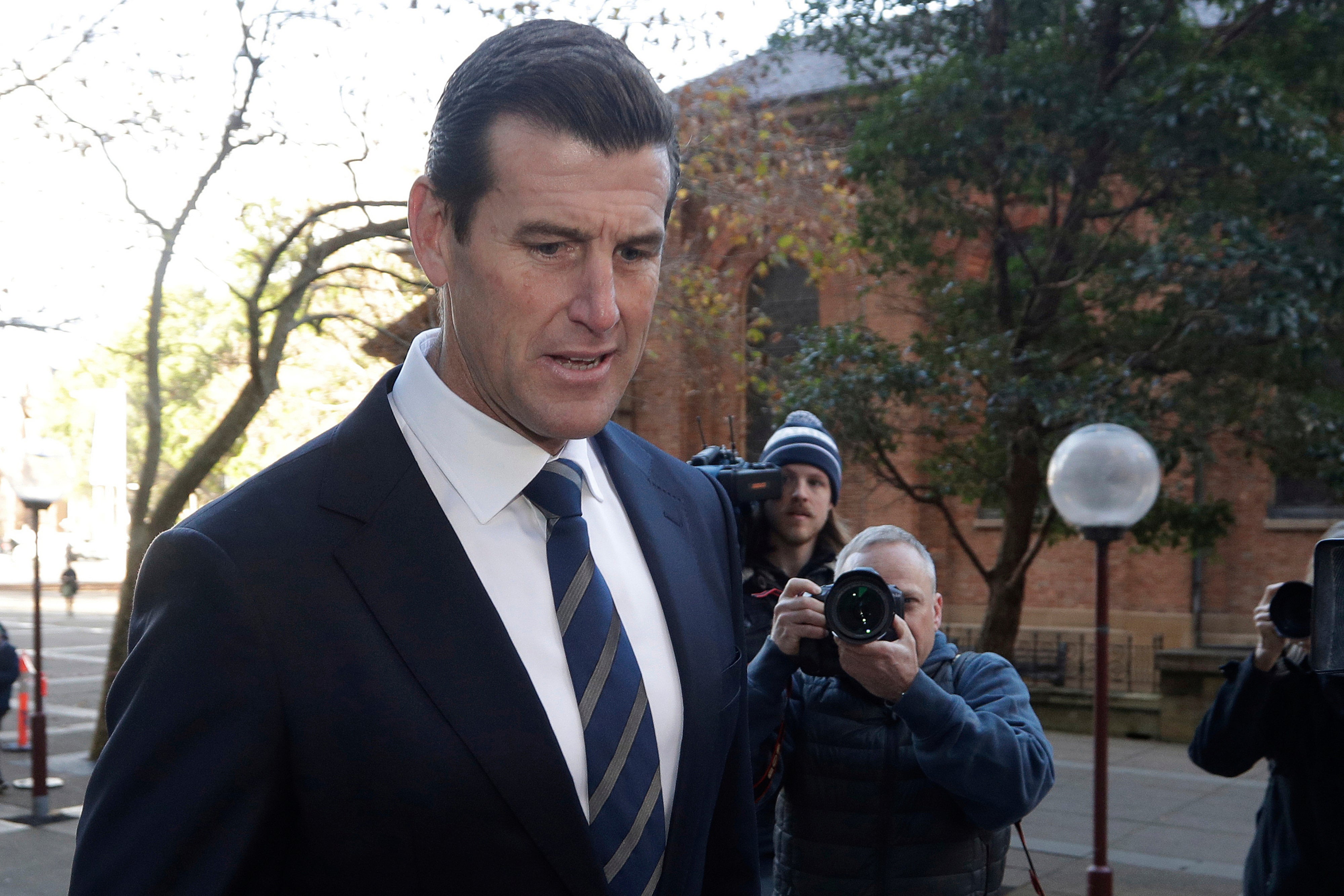 a man arrives at a courthouse followed by reporters