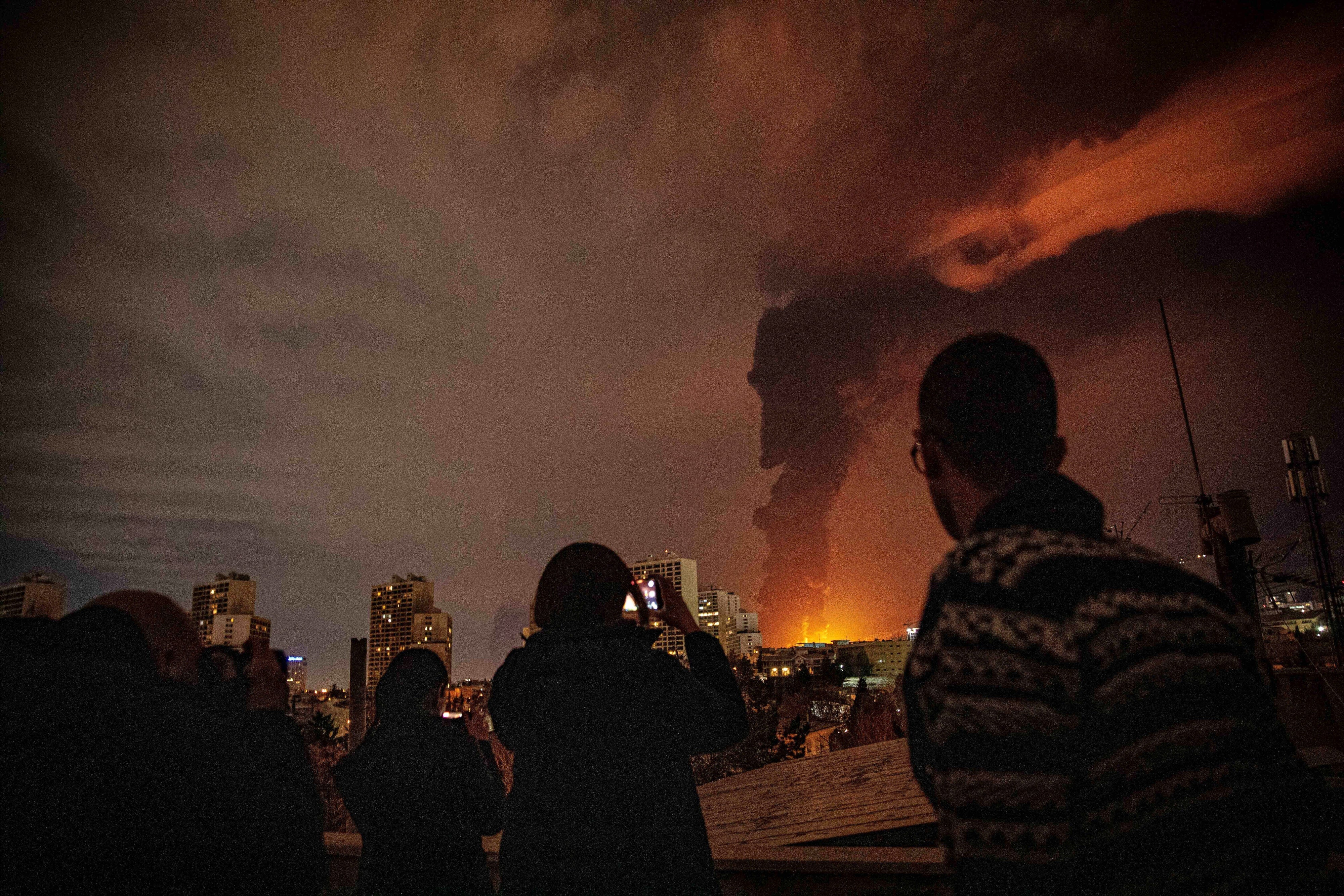Des habitants de Téhéran, en Iran, regardaient les flammes et un épais nuage de fumée noire à la suite d’une frappe aérienne israélienne contre une installation de stockage de pétrole près de la capitale, dans la nuit du 7 mars 2026.