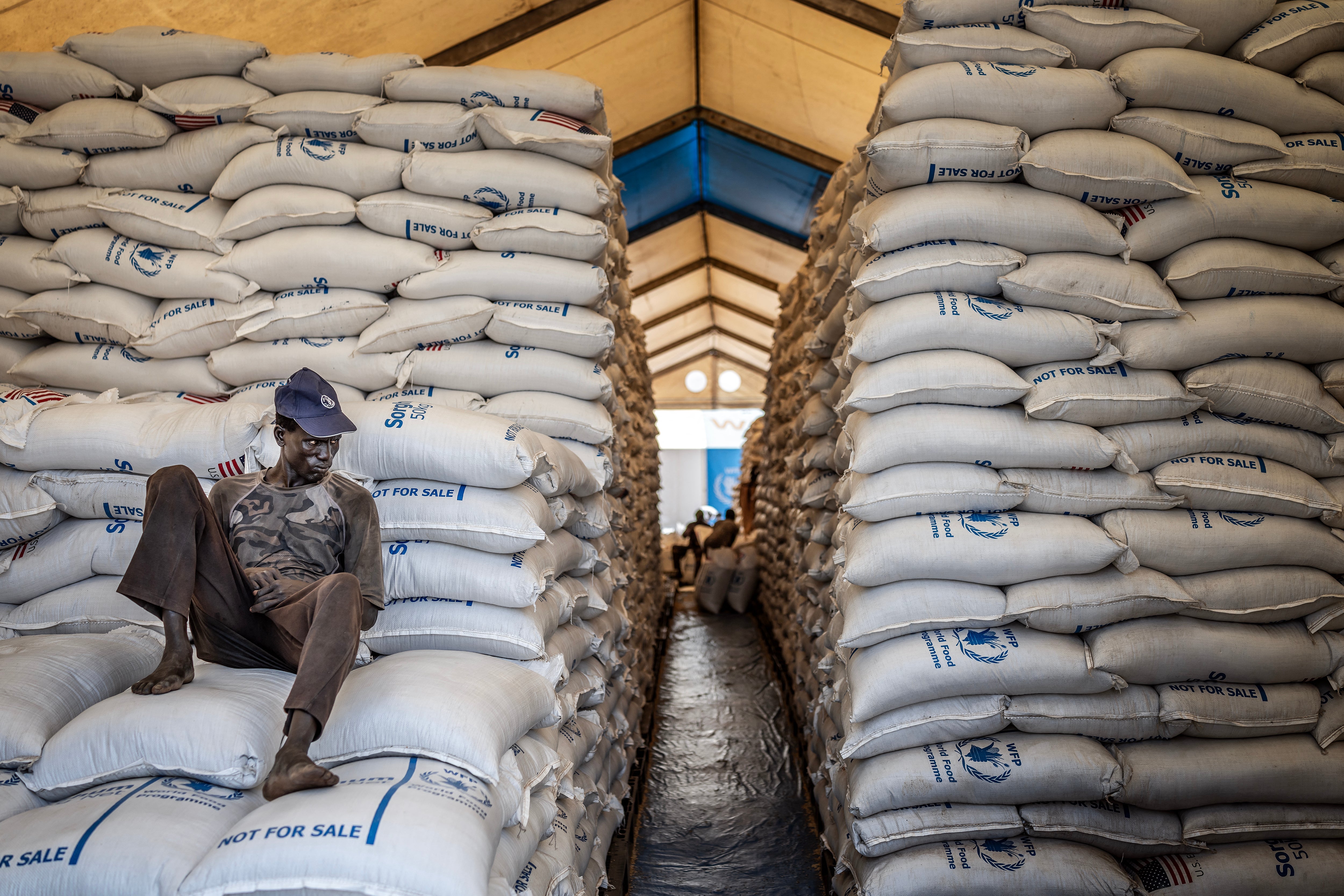 A worker sits atop sacks of food aid in a hangar where supplies are piling up because deliveries have halted because of the conflict at a World Food Programme (WFP) warehouse in Bor, Jonglei State, on February 13, 2026.
