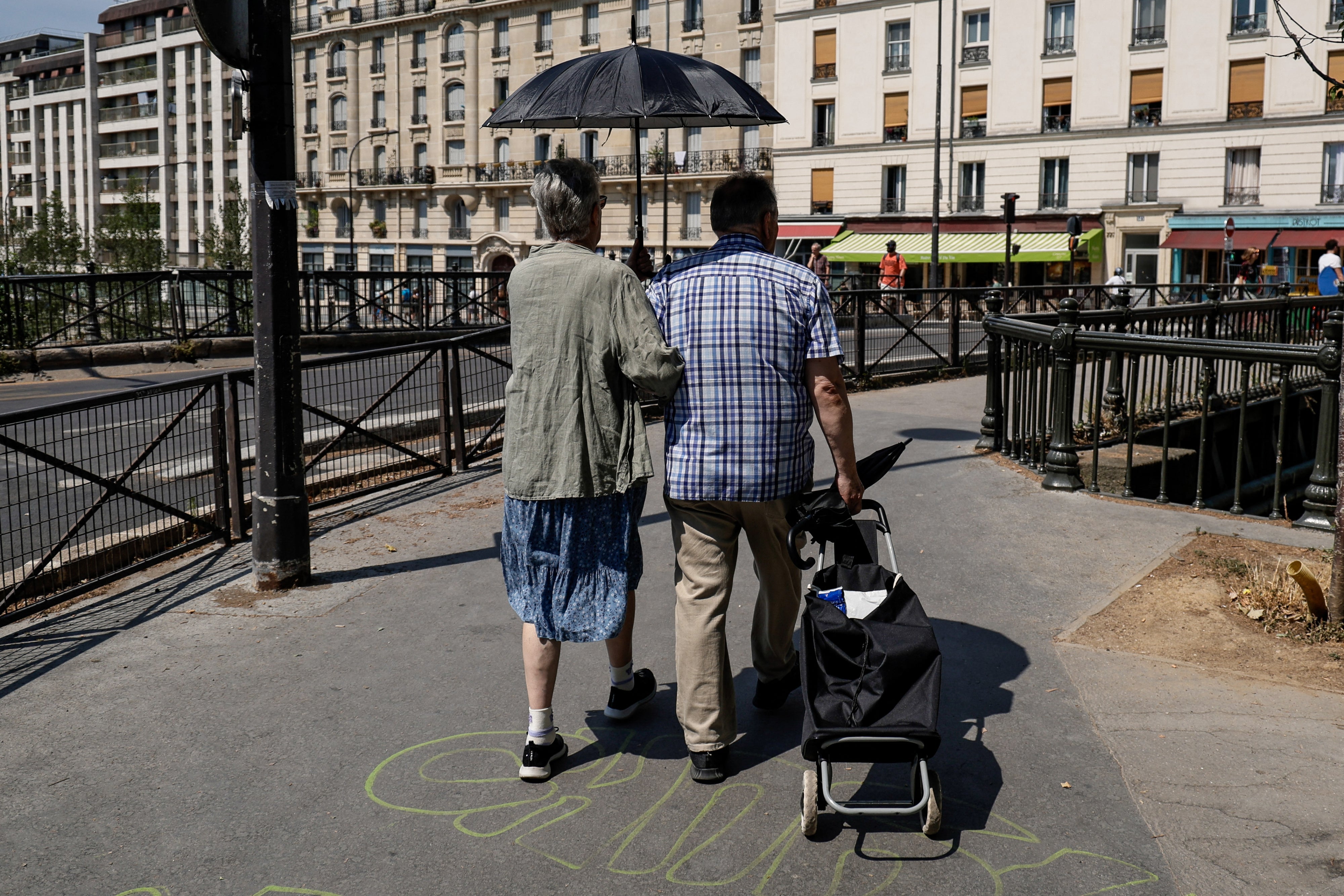 An older couple shelters from the sun under an umbrella near the Canal Saint-Martin in Paris, Ile-de-France, France, on June 26, 2026. 