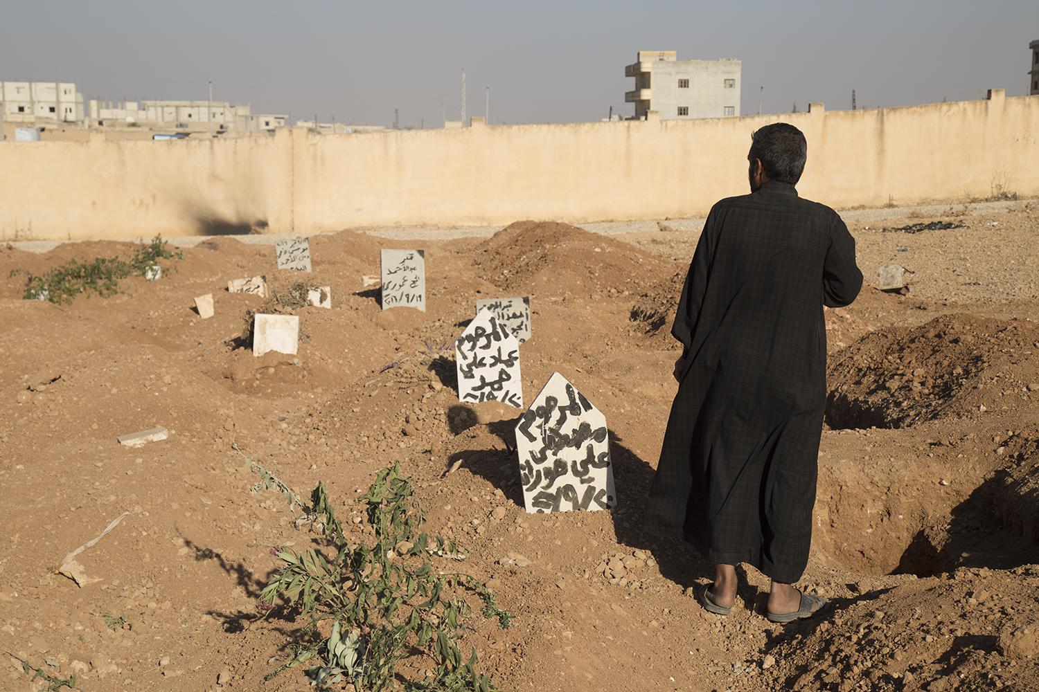A family member stands next to the graves of three children who were killed when an explosive device planted by ISIS in a school in Manbij detonated on September 27.  