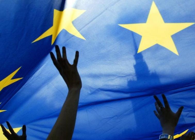People wave at a European Union flag during an EU parade, in Warsaw May 15, 2005.