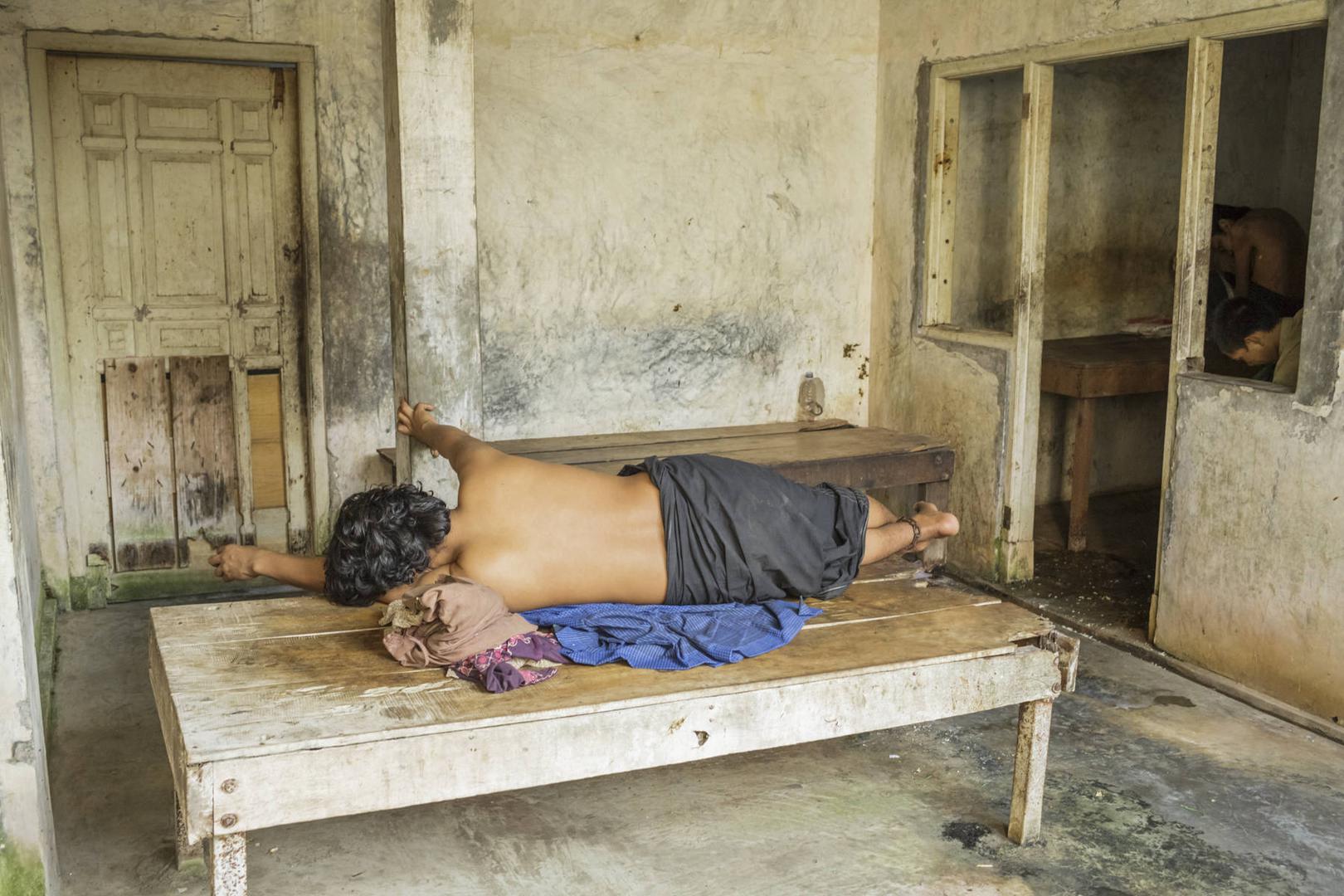 A man lying with his ankle chained to a platform bed 