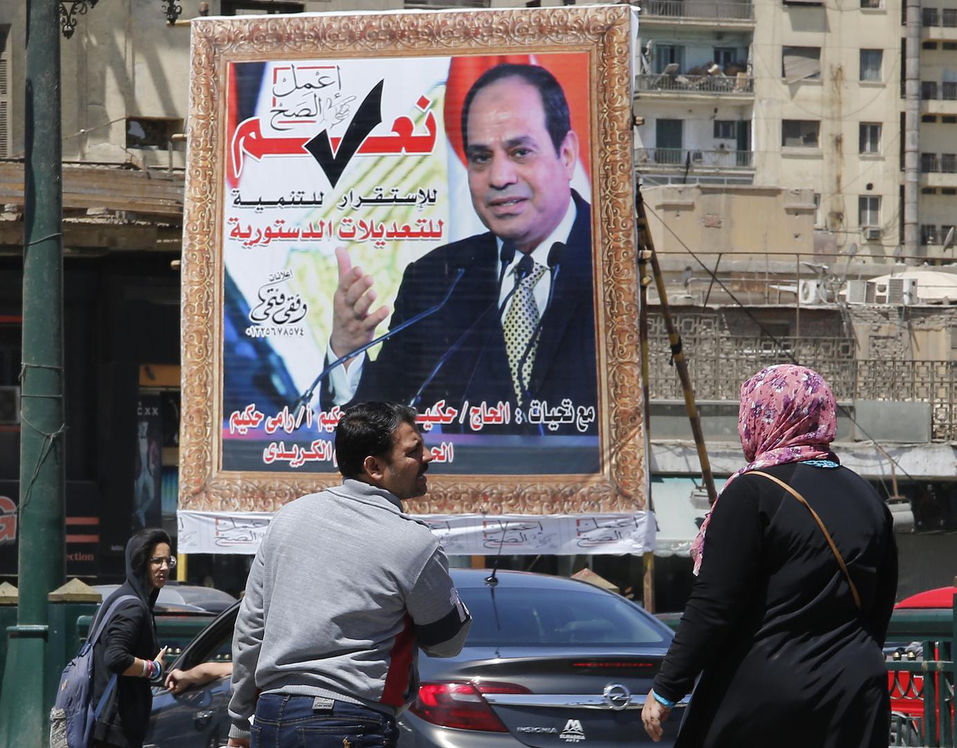 أشخاص يسيرون بجوار لافتة تدعم التعديلات في الدستور المصري، وتظهر في اللافتة صورة الرئيس المصري عبد الفتاح السيسي، القاهرة، مصر، الثلاثاء، 16 أبريل/نيسان 2019. © 2019 أسوشيتد برس/عمرو نبيل 