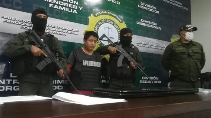 A man stands in front of a desk surrounded by armed soldiers
