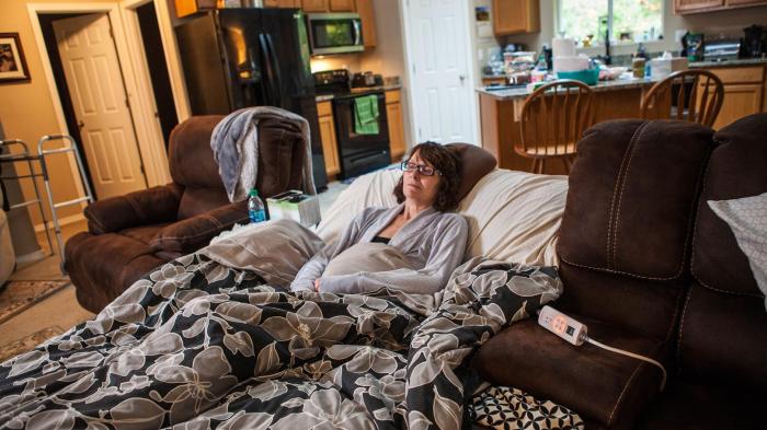 Maria Higginbotham, 57, at home in Wauna, Washington. She can only be on her feet for a few minutes at a time and needs her family to help her do simple tasks, like use the bathroom or cook a meal. 