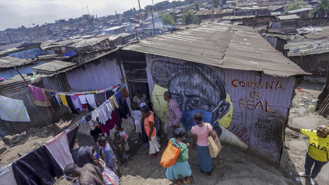 People stand outside a purple building with a mural on it that says "Corona is Real" 