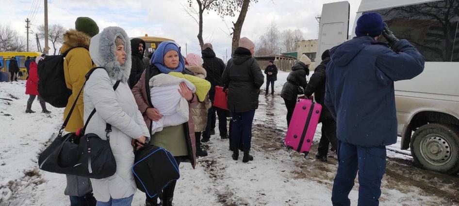 People hold their belongings as they wait to get into a van