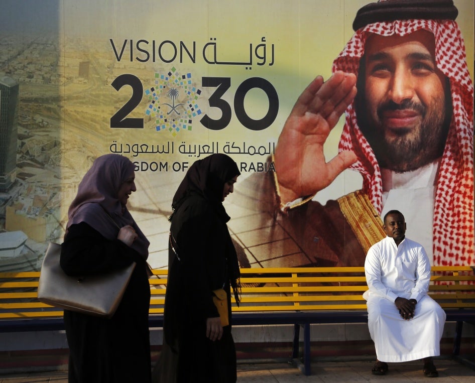 People walk past a banner showing Saudi Crown Prince Mohammed bin Salman that reads "Vision 2030"